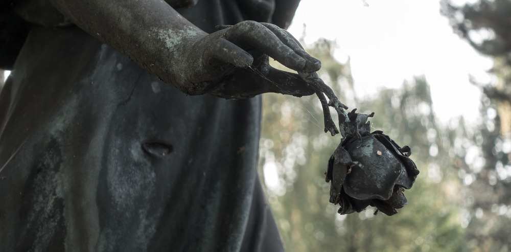 Ein Engel auf einem Friedhof hält eine Rose zum Abschied in den Hand